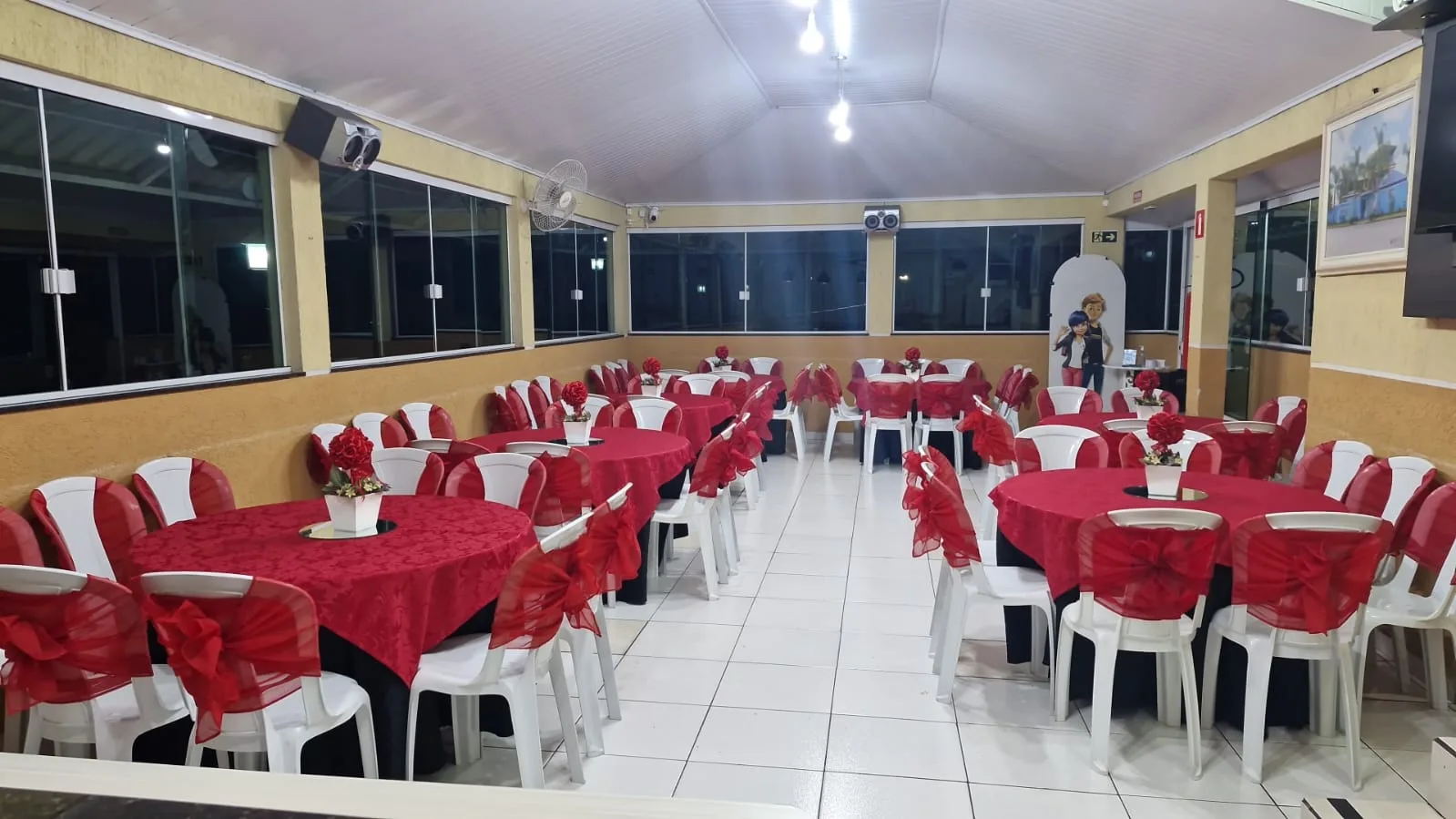 Salão superior do MinanaFest montado com mesas redondas, toalhas vermelhas e laços nas cadeiras